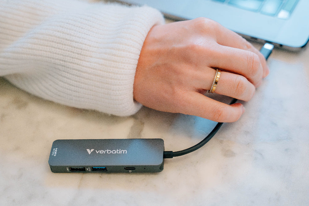 Verbatim USB hub on a marble surface with a hand holding a cable.