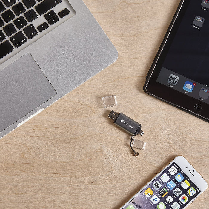 USB flash drive on a wooden surface with a laptop, smartphone, and tablet in the background.