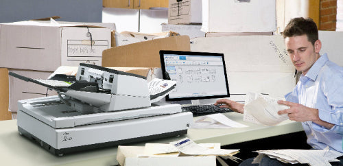 Person working at a desk with a scanner, computer, and documents